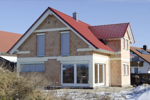 Rohbau eines Einfamilienhauses mit rotem Ziegeldach und weißen Fenstern im Schnee